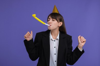 Woman in party hat with blower on purple background