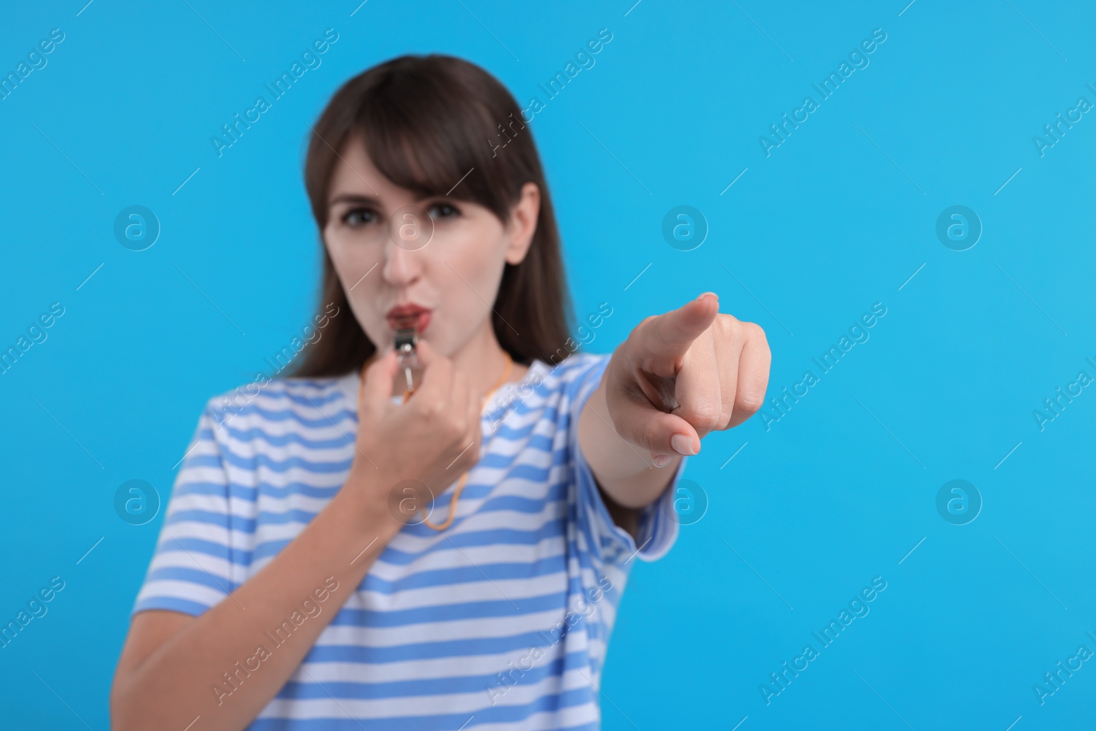 Photo of Woman blowing whistle on light blue background, selective focus. Space for text