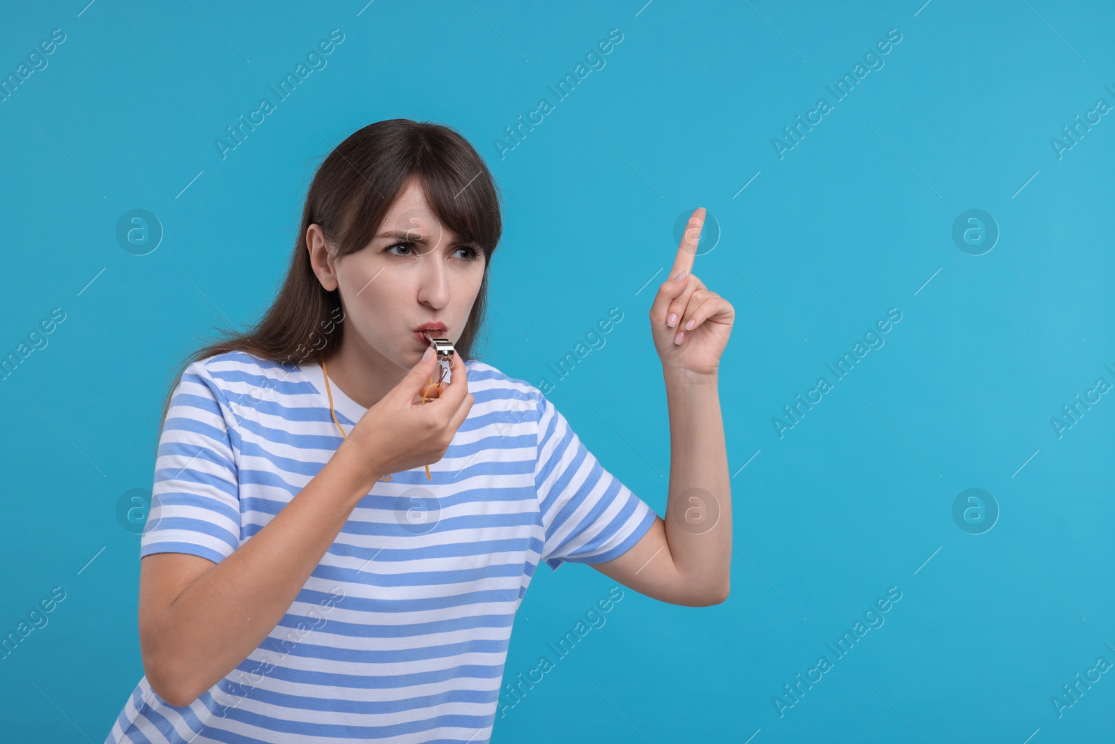 Photo of Woman blowing whistle on light blue background, space for text