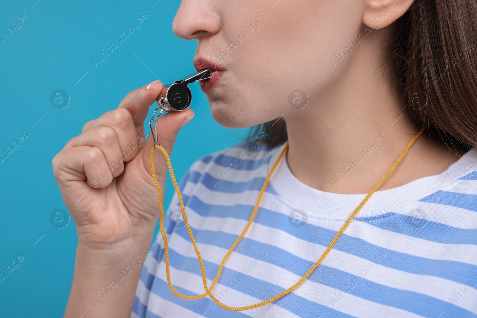 Photo of Woman blowing whistle on light blue background, closeup