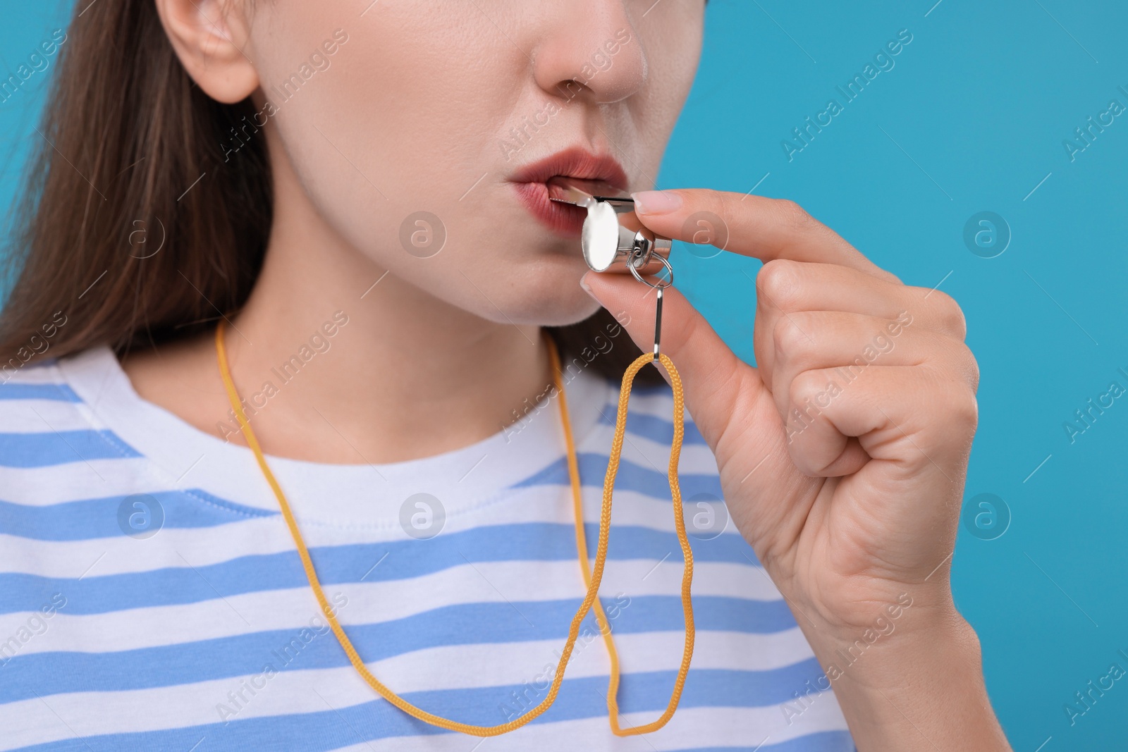 Photo of Woman blowing whistle on light blue background, closeup