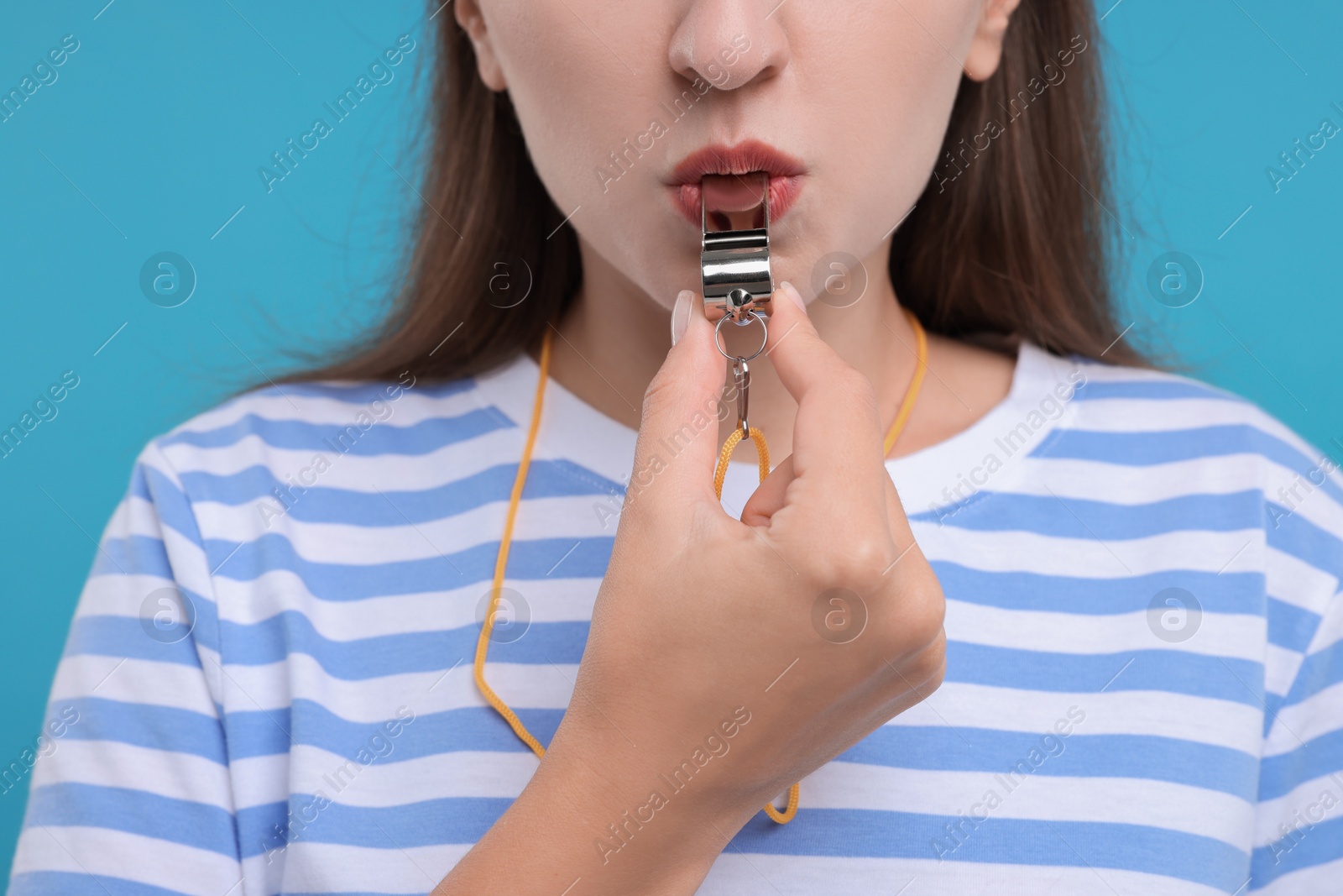 Photo of Woman blowing whistle on light blue background, closeup