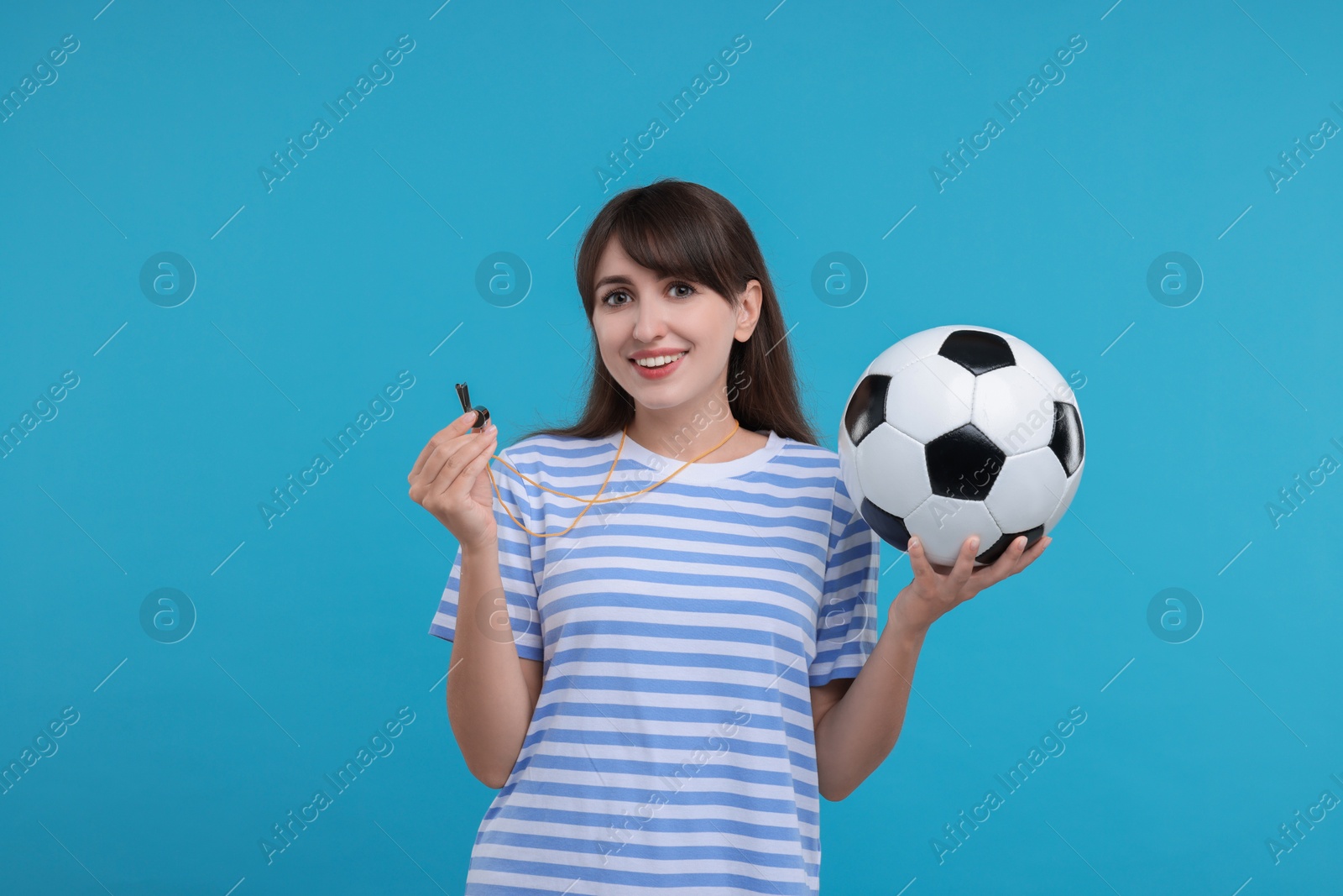 Photo of Happy woman with whistle and soccer ball on light blue background