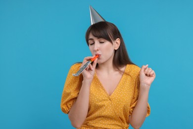 Photo of Woman in party hat with blower on light blue background