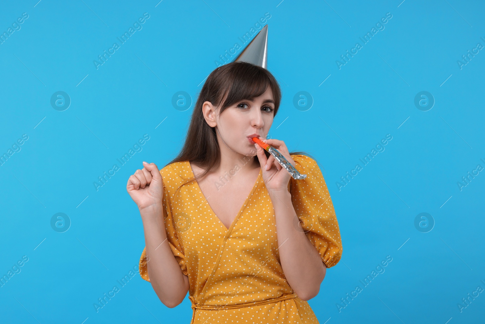 Photo of Woman in party hat with blower on light blue background