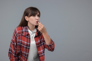 Woman blowing whistle on grey background, space for text