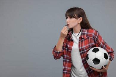 Woman with soccer ball blowing whistle on grey background, space for text