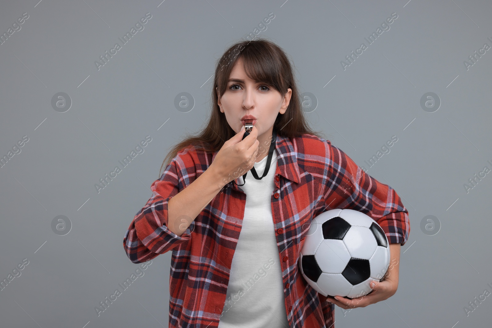 Photo of Woman with soccer ball blowing whistle on grey background