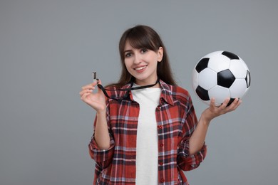 Happy woman with whistle and soccer bal on grey background