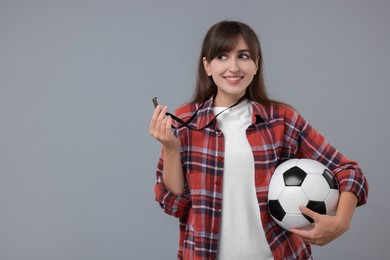 Happy woman with whistle and soccer bal on grey background, space for text