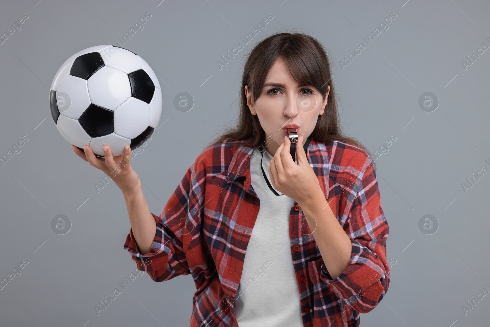 Photo of Woman with soccer ball blowing whistle on grey background