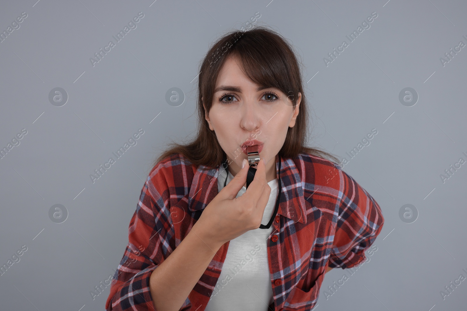 Photo of Young woman blowing whistle on grey background