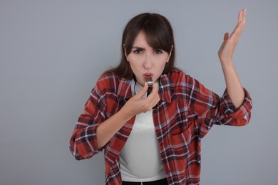 Young woman blowing whistle on grey background