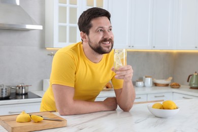 Happy man holding glass of water with lemon in kitchen