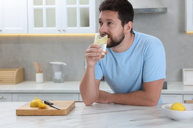 Handsome man drinking water with lemon at white marble table in kitchen