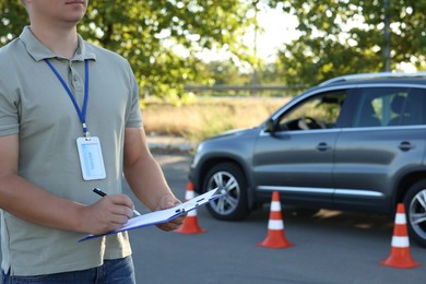 Examiner with clipboard during exam at driving school test track, closeup