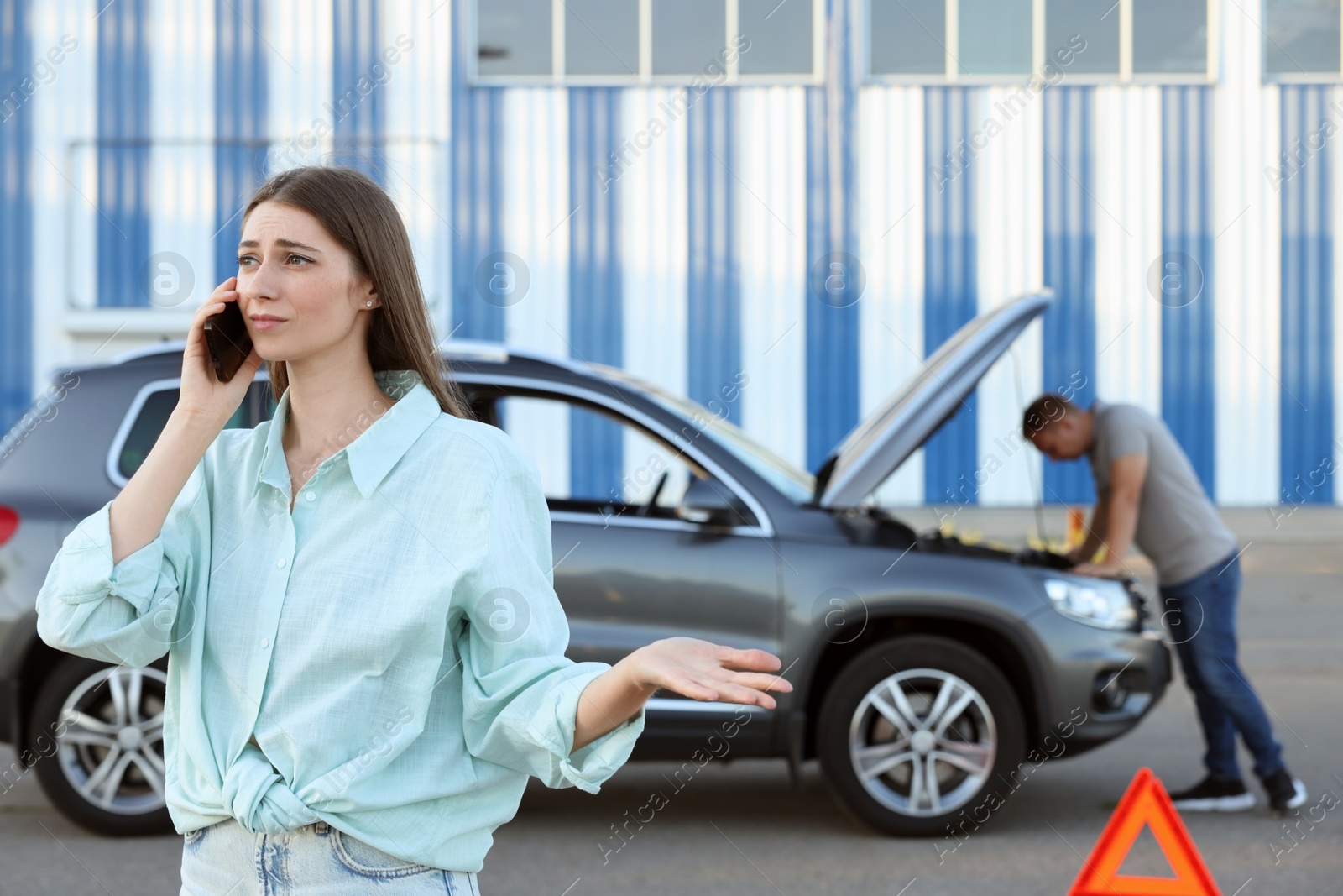 Photo of Man standing near broken auto while woman calling to car service outdoors