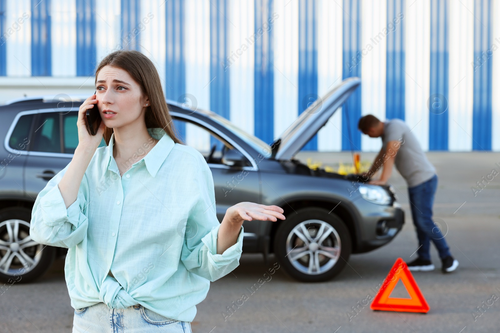 Photo of Man standing near broken auto while woman calling to car service outdoors