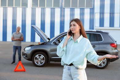 Man standing near broken auto while woman calling to car service outdoors