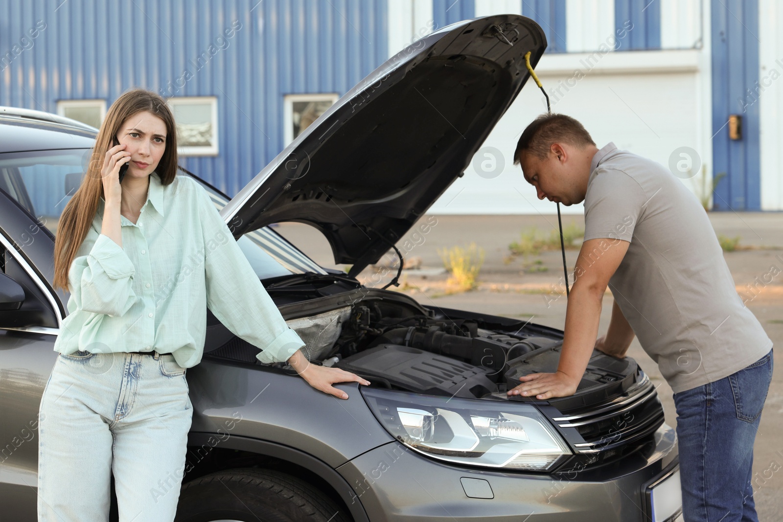 Photo of Man examining broken auto while woman calling to car service outdoors