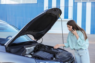 Stressed woman talking on phone near broken car outdoors