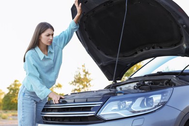 Photo of Stressed woman looking under hood of broken car outdoors