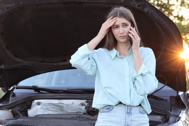 Stressed woman talking on phone near broken car outdoors