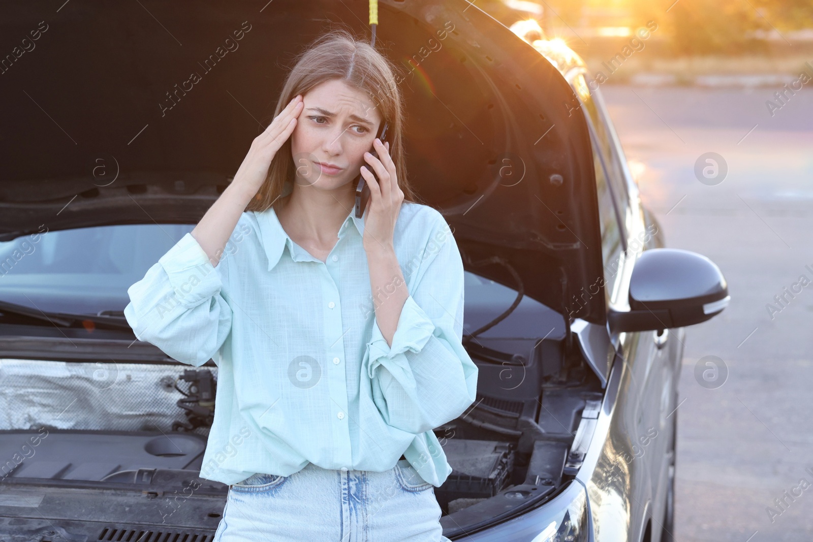 Photo of Stressed woman talking on phone near broken car outdoors