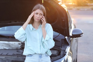 Photo of Stressed woman talking on phone near broken car outdoors