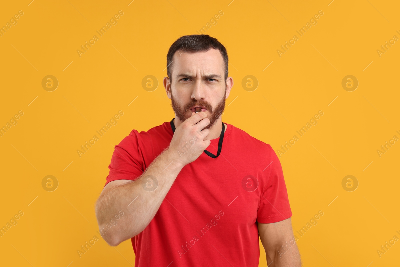 Photo of Young man blowing whistle on orange background