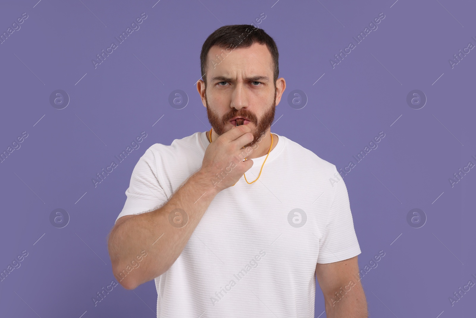 Photo of Young man blowing whistle on purple background