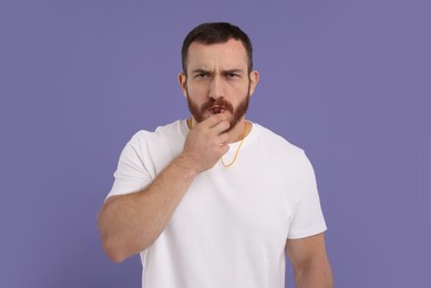 Young man blowing whistle on purple background