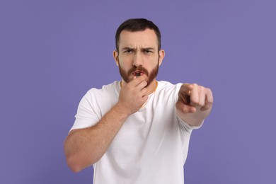 Young man blowing whistle on purple background