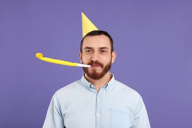 Photo of Man in party hat with blower on purple background