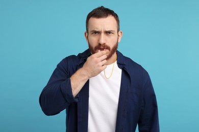 Photo of Young man blowing whistle on light blue background