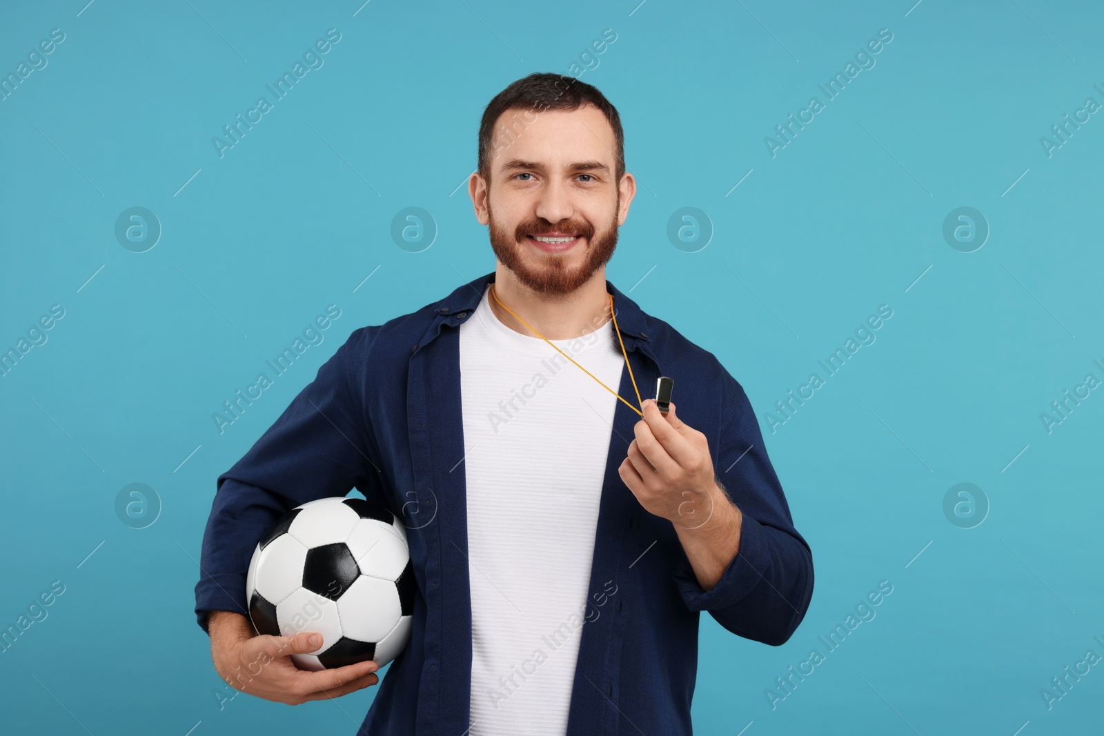 Photo of Happy young man with whistle and soccer ball on light blue background