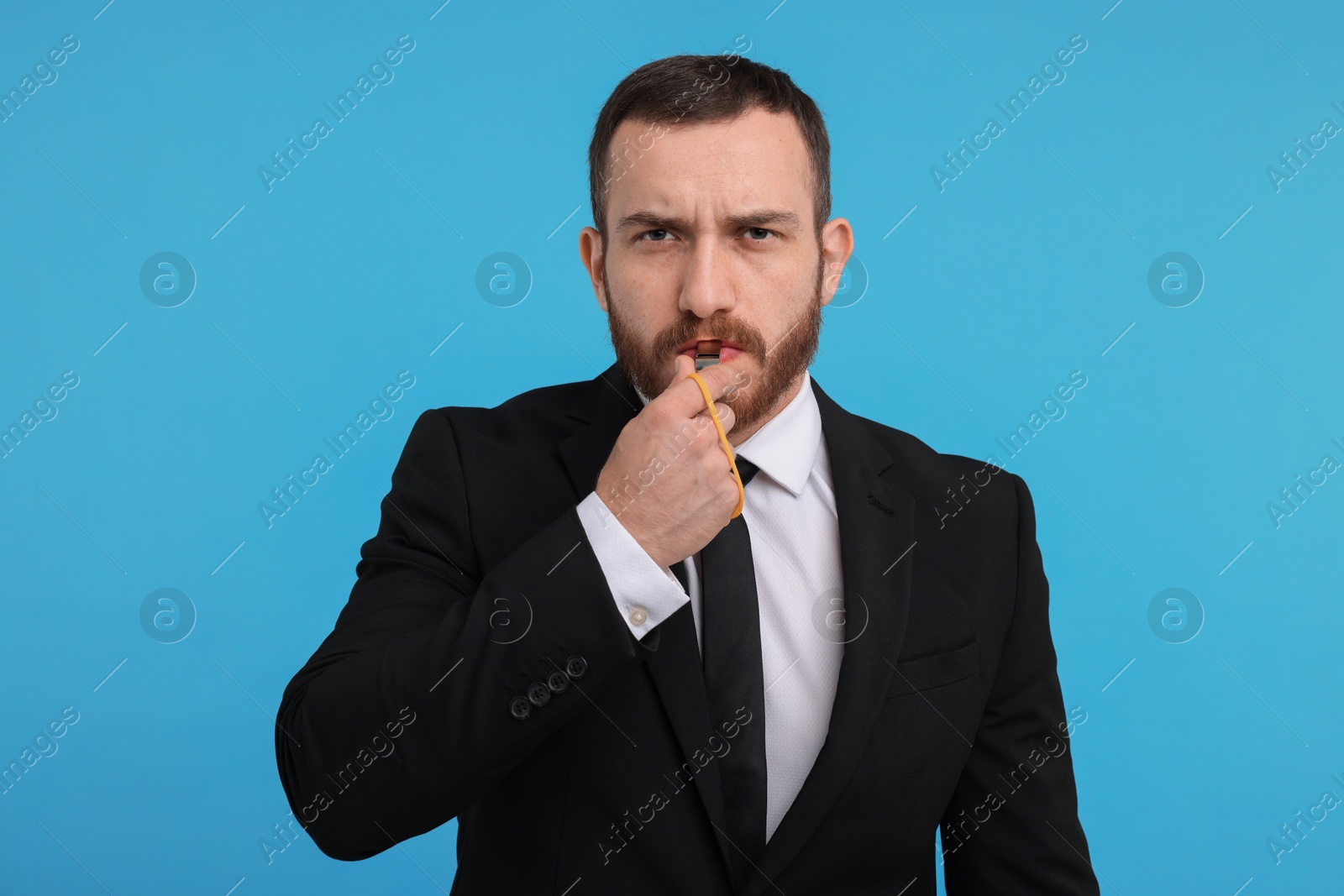 Photo of Young man blowing whistle on light blue background