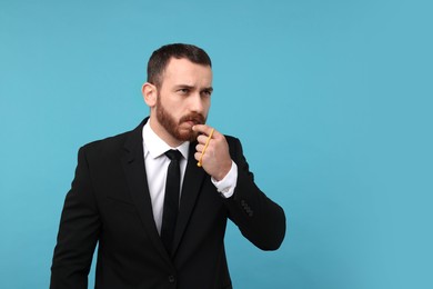 Photo of Young man blowing whistle on light blue background, space for text