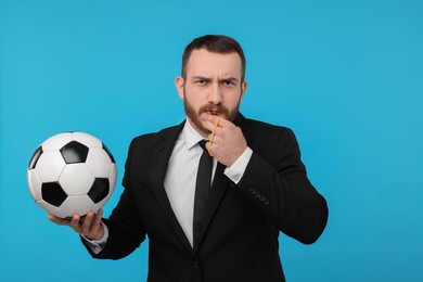 Photo of Young man with soccer ball blowing whistle on light blue background