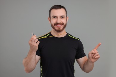 Happy young man with whistle on grey background