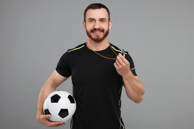 Photo of Happy young man with whistle and soccer ball on grey background