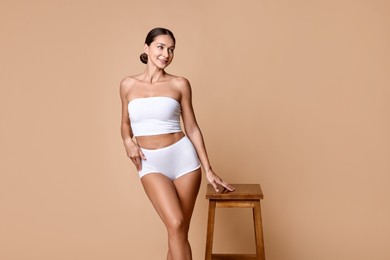 Smiling woman with perfect skin in underwear posing with stool against beige background. Body care