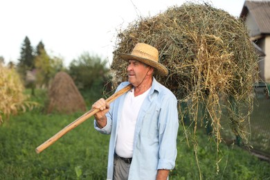 Senior man in straw with pile of hay on pitchfork at farm