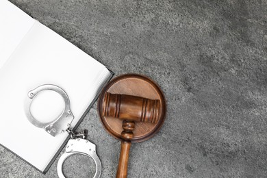 Photo of Book, judge's gavel and handcuffs on gray textured table, flat lay. Space for text