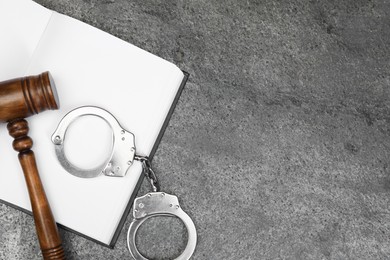 Book, judge's gavel and handcuffs on gray textured table, flat lay. Space for text