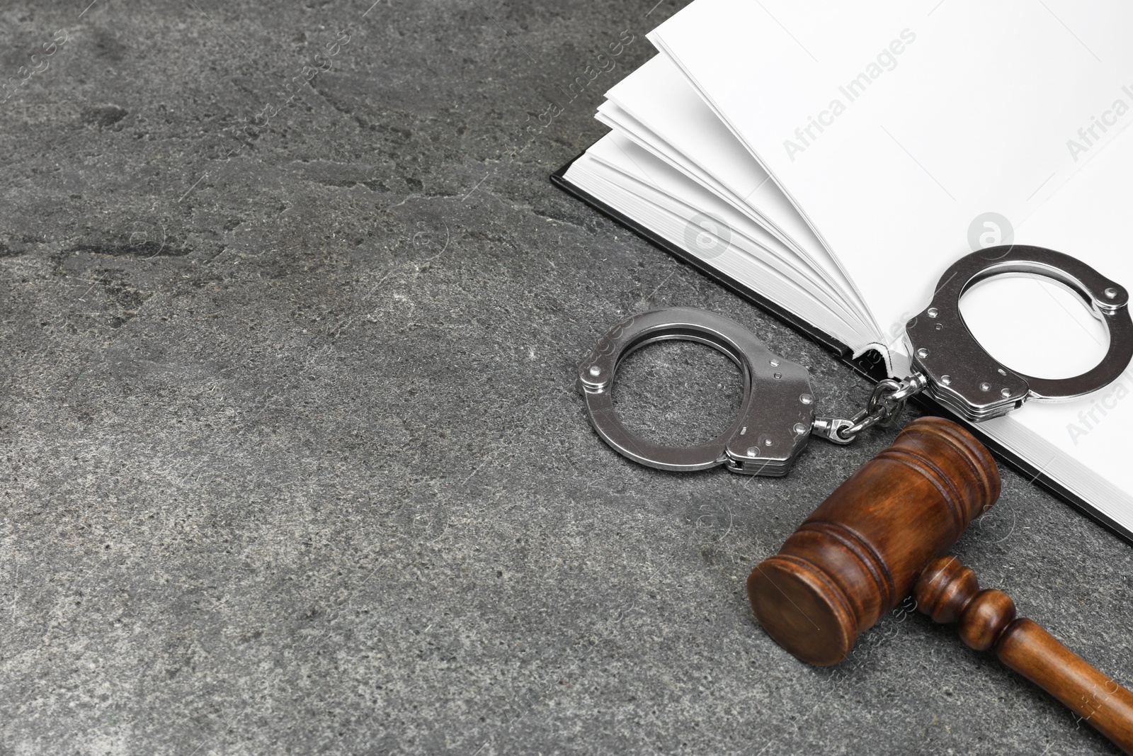 Photo of Book, judge's gavel and handcuffs on gray textured table, space for text