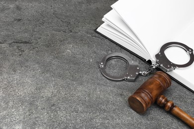 Book, judge's gavel and handcuffs on gray textured table, space for text