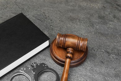 Book, judge's gavel and handcuffs on gray textured table, space for text