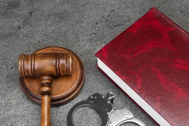 Book, judge's gavel and handcuffs on gray textured table