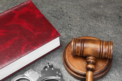 Book, judge's gavel and handcuffs on gray textured table